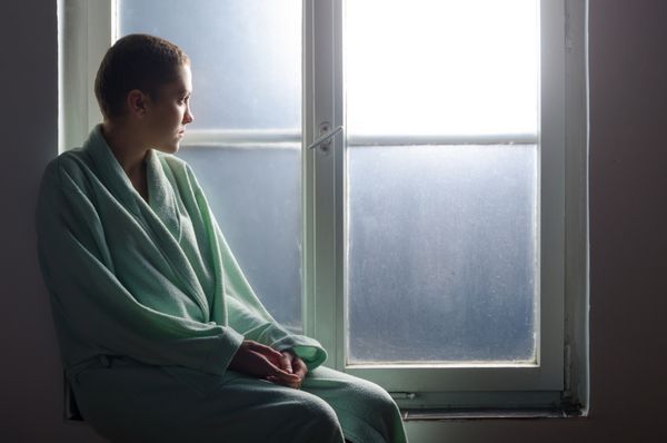 بیمار جوان سرطانی که جلوی پنجره بیمارستان نشسته است
