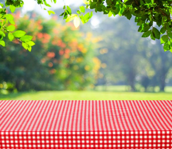 میز خالی و رومیزی قرمز با پس‌زمینه بوکه برگ‌های سبز تار برای مونتاژ نمایش محصول