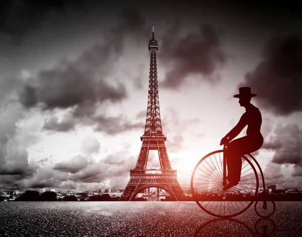 مردی سوار بر دوچرخه رترو در کنار برج افل پاریس فرانسه سیاه و سفید حال و هوای قدیمی و نور خورشید قرمز