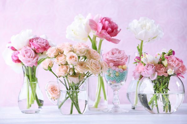 گل های زیبای بهاری در گلدان های شیشه ای در زمینه صورتی روشن