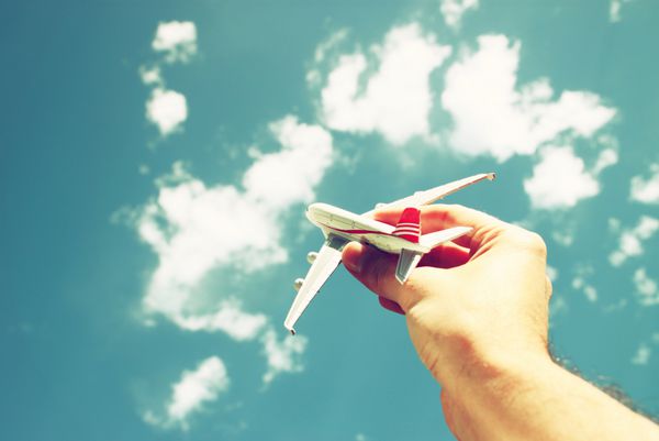 دست مردی که هواپیمای اسباب‌بازی را در مقابل آسمان آبی با ابرها در دست گرفته است تصویر فیلتر شده