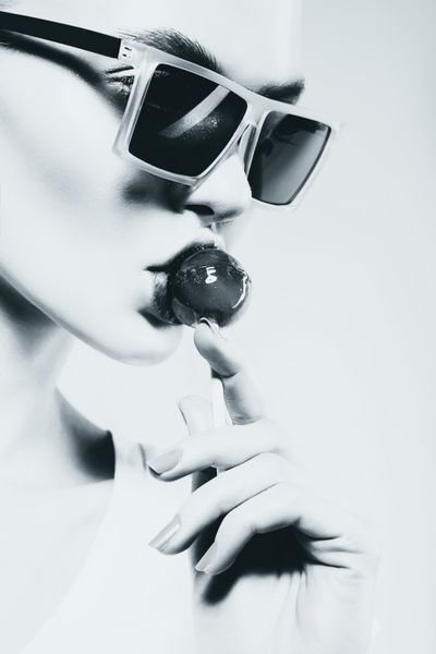 زن جذاب تک رنگ در حال خوردن آبنبات چوبی با عینک آفتابی