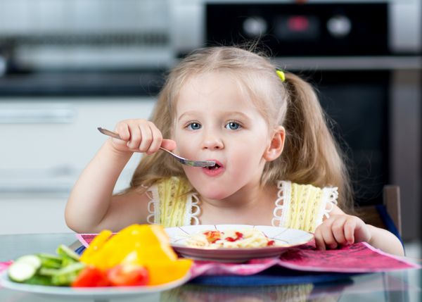 بچه در حال خوردن اسپاگتی با سبزیجات در مهد کودک یا خانه