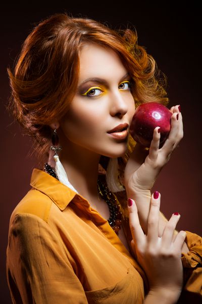زن جوان زیبا با آرایش زرد روشن با لباس پاییزی نارنجی که سیب قرمز را در دست دارد