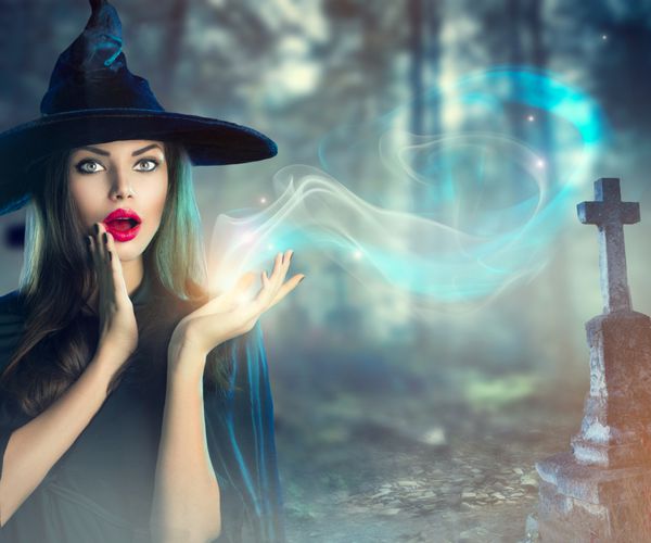جادوگر هالووین با جادو در یک گورستان شبح وار قدیمی تاریک زن جوان زیبا با کلاه و لباس جادوگر که نور جادویی را در دست دارد طراحی هنری هالووین