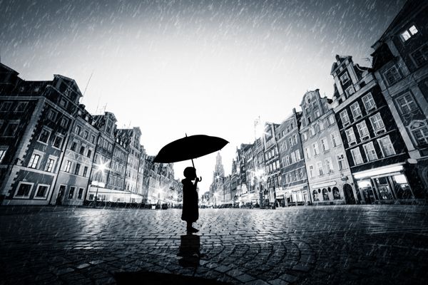 کودکی با چتر که به تنهایی روی شهر قدیمی سنگفرش زیر باران ایستاده است مفهوم گم شدن تنهایی در یک دنیای بزرگ یا کاوش