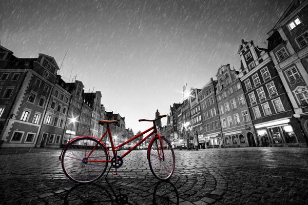 دوچرخه قرمز قدیمی در شهر قدیمی سنگفرش شده در باران رنگ در سیاه و سفید میدان بازار در شب وروتسواو لهستان