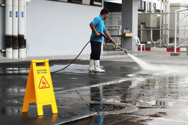 احتیاط بنر کف مرطوب و تمیز کردن زمین کارگر با پس زمینه دستگاه فشار قوی هوا