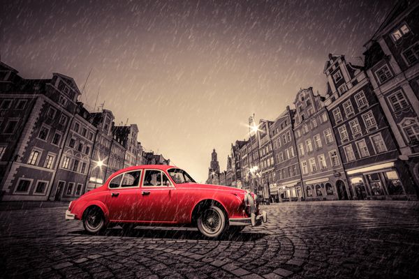 ماشین قرمز رترو در شهر قدیمی سنگفرش شده در باران میدان بازار در شب وروتسواو لهستان