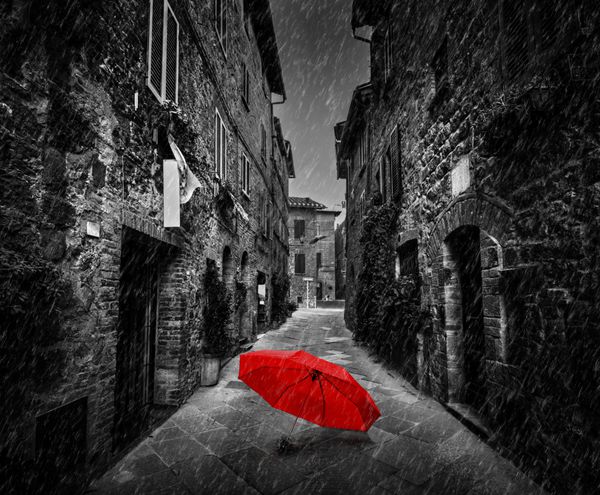 چتر در خیابان باریک تاریک در یک شهر قدیمی ایتالیایی در توسکانی ایتالیا باران سیاه و سفید با قرمز