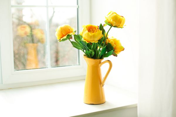 گل های زرد در یک گلدان زرد روی طاقچه