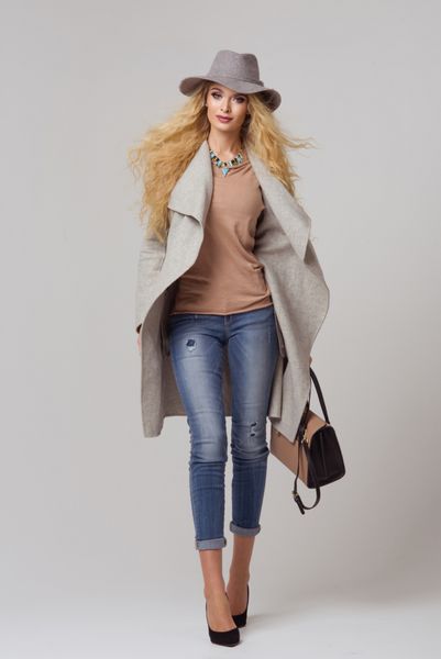 مدل بلوند مد با لباس های زیبا که در استودیو ژست می گیرد پوشیدن کت کلاه کیف دستی شلوار جین پاره