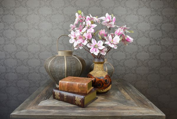 طبیعت بی جان با شکوفه ماگنولیا کتاب های قدیمی و فانوس روی میز چوبی روستایی
