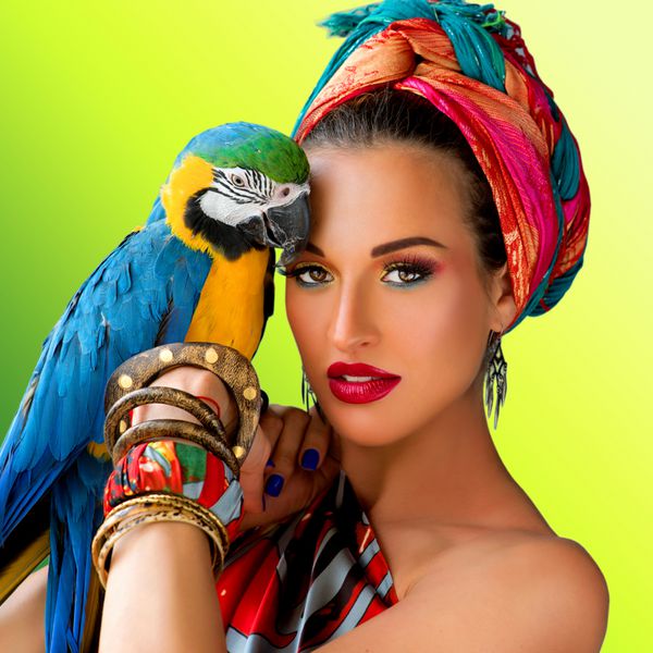 پرتره زن جوان جذاب به سبک آفریقایی با طوطی آرا روی دستش در زمینه رنگارنگ