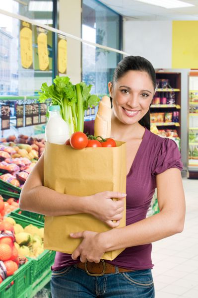 زن جوانی که یک کیسه مواد غذایی پر از مواد غذایی تازه و سالم در سوپرمارکت در دست دارد