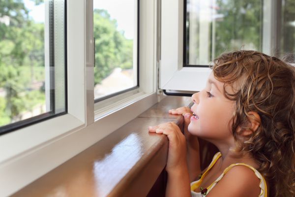 دختر کوچک خندان زیبا در بالکن از پنجره نگاه کنید