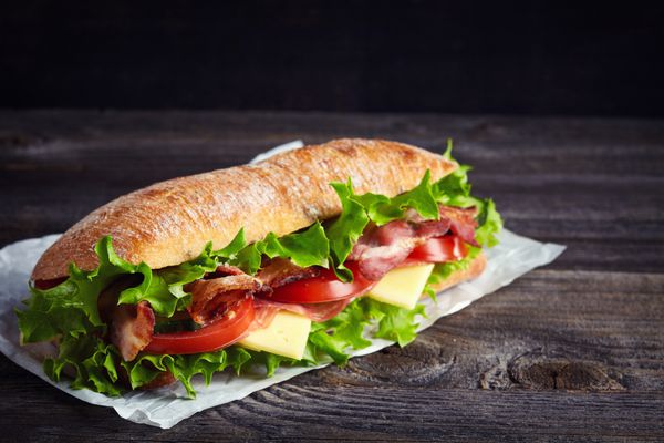 ساندویچ زیردریایی تازه با ژامبون پنیر بیکن گوجه فرنگی خیار کاهو و پیاز در زمینه چوبی تیره