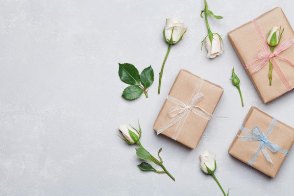 جعبه هدیه یا هدیه پیچیده شده در کاغذ کرافت و گل رز روی میز خاکستری از بالا یک ظاهر طراحی شده تخت sp را برای متن کپی کنید