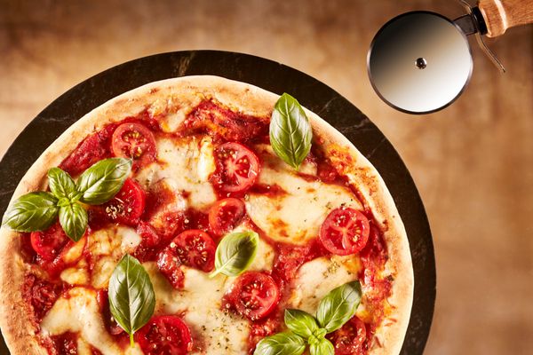 پیتزا ایتالیایی مارگریتا تازه پخته شده با پنیر موزارلا گوجه فرنگی و ریحان تازه روی پوسته ضخیم نمای بالای صفحه روی بشقاب با چرخ شیرینی برای برش