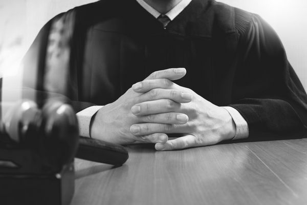 مفهوم عدالت و قانون قاضی مرد در یک دادگاه در حال ضربه زدن به سنگر کار با رایانه لوحی دیجیتالی که صفحه کلید روی میز چوبی قرار دارد سیاه و سفید