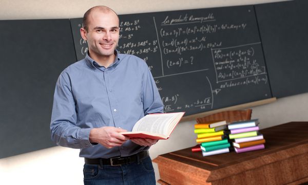 معلم مرد جوانی که در کلاس ریاضی کتابی در دست دارد