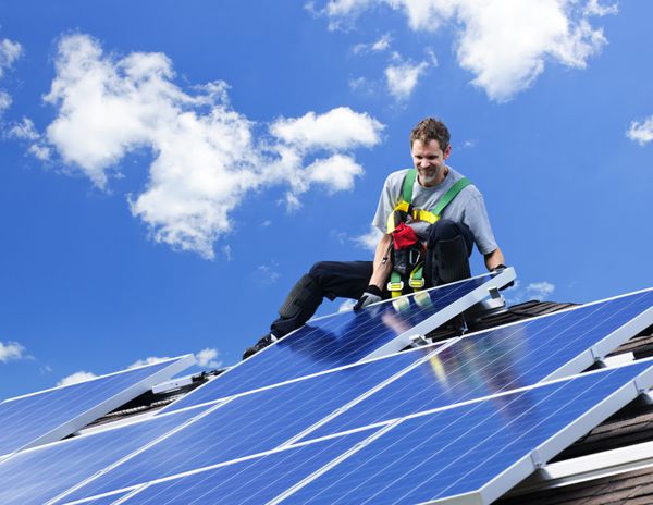 کارگری که در حال نصب پنل های خورشیدی پوولتائیک انرژی جایگزین روی پشت بام است
