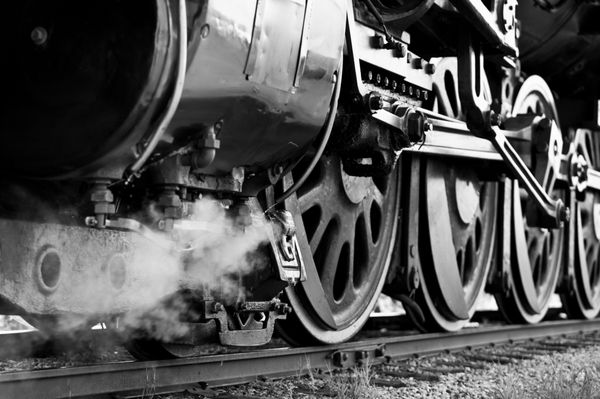 نمای نزدیک سیاه و سفید از چرخ ها در یک قطار بخار قدیمی که منتظر ترک ایستگاه است