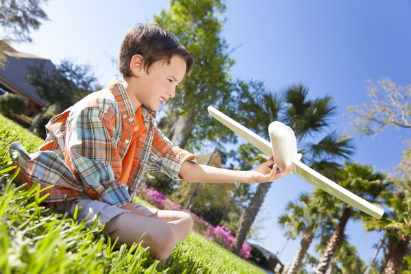 پسر جوانی با هواپیمای مدل اسباب بازی روی چمن بیرون نشسته است