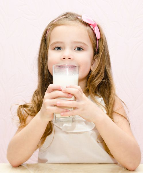 دختر کوچک خندان زیبا در حال نوشیدن شیر