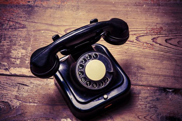 تلفن مشکی قدیمی با گرد و غبار و خط و خش روی کف چوبی