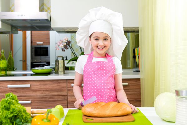 دختر کوچولو با پیش بند صورتی در حال بریدن نان