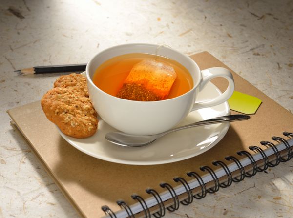 فنجان چای با چای کیسه ای و کلوچه در دفترچه یادداشت