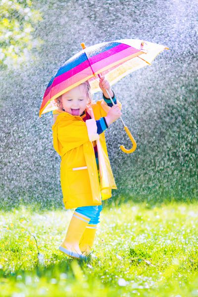 کودک نوپا بامزه با چتر بازی در باران