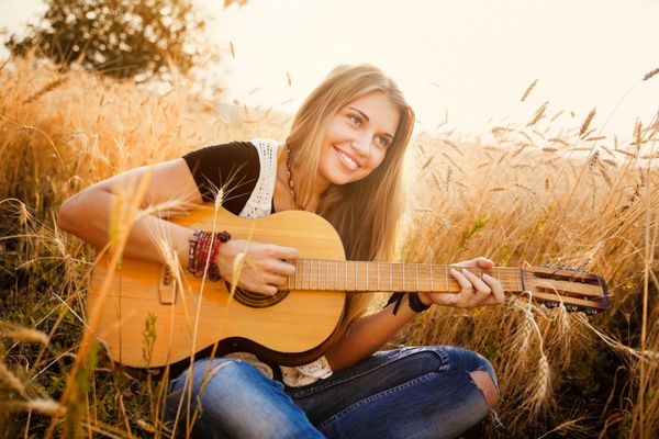 دختر زیبا در حال نواختن گیتار در گندم زار