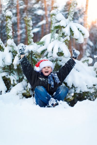 پسر شاد در کلاه بابا نوئل در جنگل زمستانی