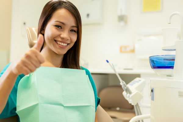 زن آسیایی خندان کنار دندانپزشک نشسته و به سمت او لبخند می زند