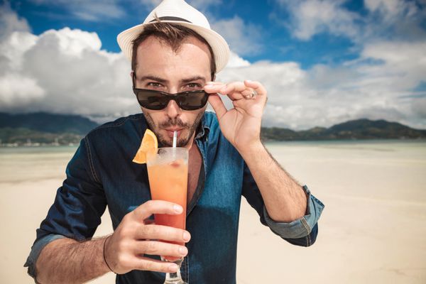 مردی در ساحل در حال نوشیدن یک کوکتل پرتقالی