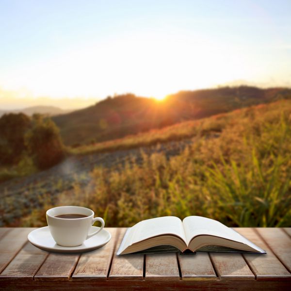 یک فنجان قهوه و یک کتاب روی میز چوبی