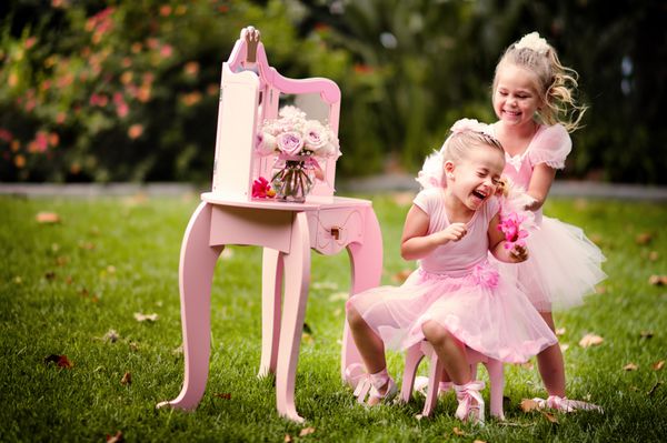 دو دختر کوچولوی شاد که لباس های پرنسس به تن دارند در یک باغ زیبا سرگرم می شوند