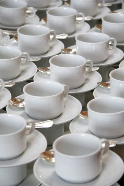 پشته های فنجان قهوه روی نعلبکی با قاشق چای خوری نقره ای