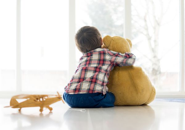 کودک کوچکی که در اتاق نشیمن با خرس عروسکی نشسته است
