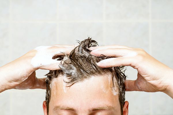 مرد جوانی که موهایش را می‌شوید دوش می‌گیرد و کف روی سرش دارد انگشت‌هایش را در موهایش نگه می‌دارد