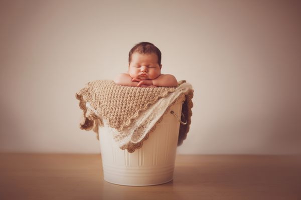 نوزاد شاد و ناز با کلاه بافتنی آبی که در یک سبد خوابیده است