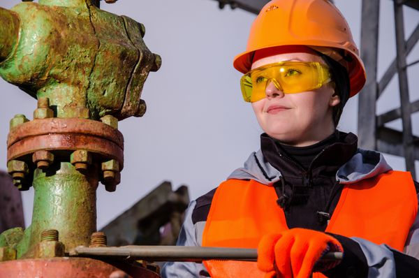 مهندس زن در میدان نفت در حال تعمیر سر چاه با آچار با کلاه ایمنی نارنجی و لباس کار مفهوم نفت و گاز