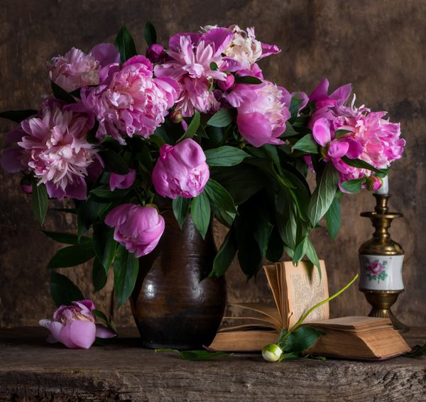 طبیعت بی جان هنری با گل صد تومانی در گلدان و کتاب روی زمینه چوبی