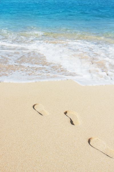 چاپ پا در ساحل شنی با موج آبی ملایم اقیانوس در پس زمینه تمرکز انتخابی