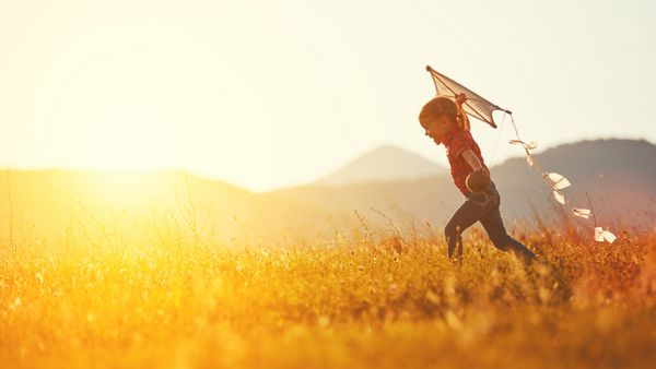 دختر بچه شاد با بادبادکی که در تابستان در طبیعت روی چمنزار می دود
