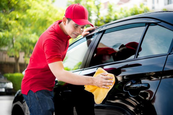 کارکنان خدمات خودرو در ماشین تمیز کردن یکنواخت قرمز با پارچه میکروفیبر - جزئیات ماشین و مفاهیم نوبت دهی