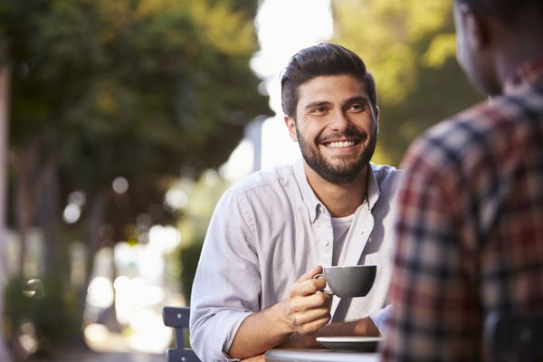 دو دوست مرد بالغ بیرون کافه نشسته اند و مشغول صحبت کردن با قهوه هستند