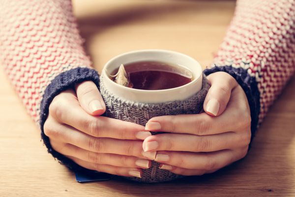 لیوان چای گرم کننده دست های زن در جامپر پشمی رترو میز چوبی
